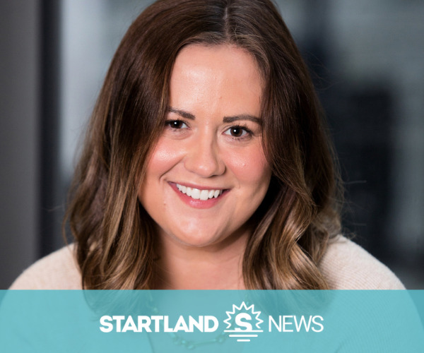 Woman with shoulder-length brown hair smiling at the camera, seated indoors against a blurred background; teal lower banner reads: STARTLAND [S logo] NEWS.
